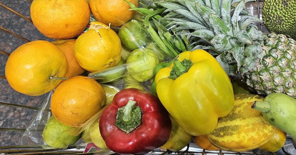 Shopping trolley filled with IBS-friendly produce including oranges, lemons, red and yellow bell peppers, pineapple, papaya and chayote